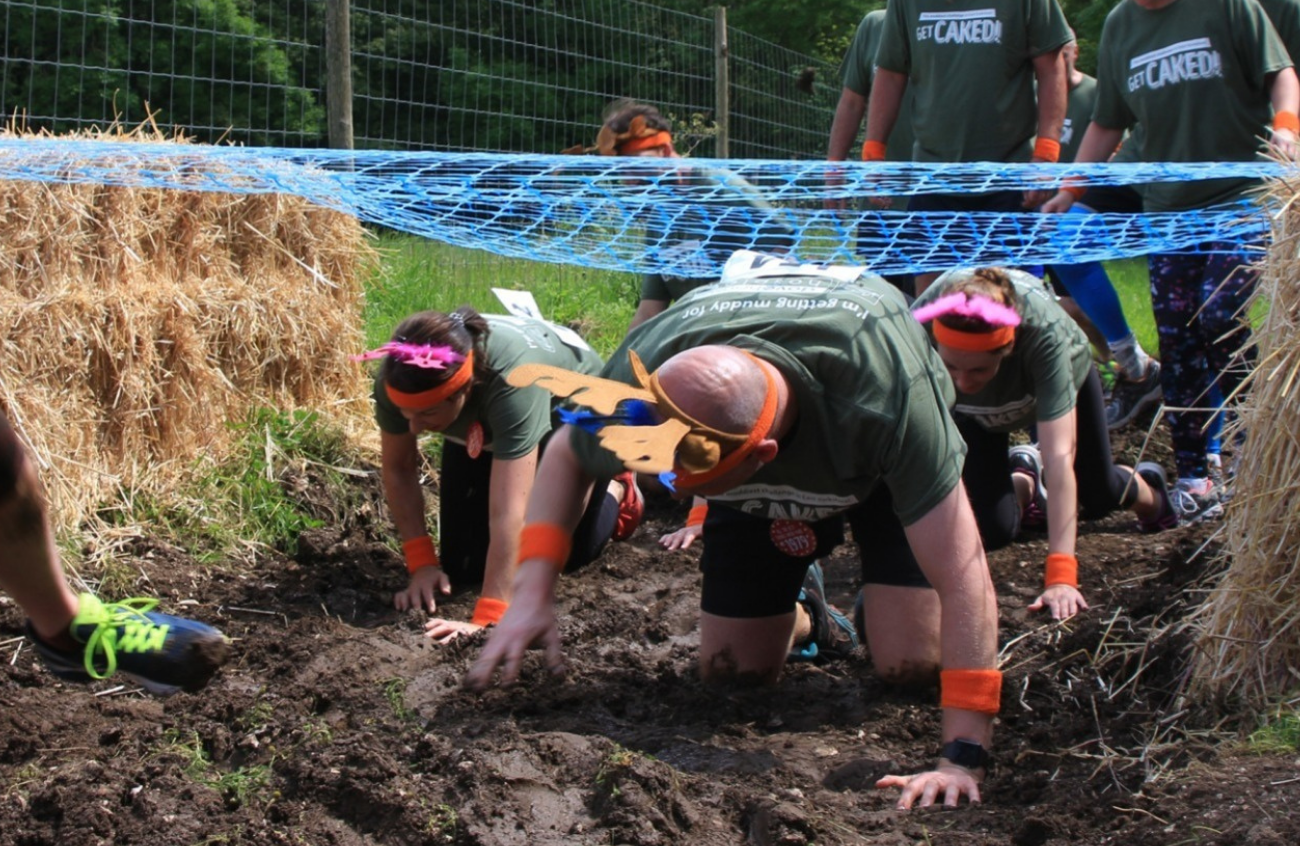 A group of people crawl under a net in the mud